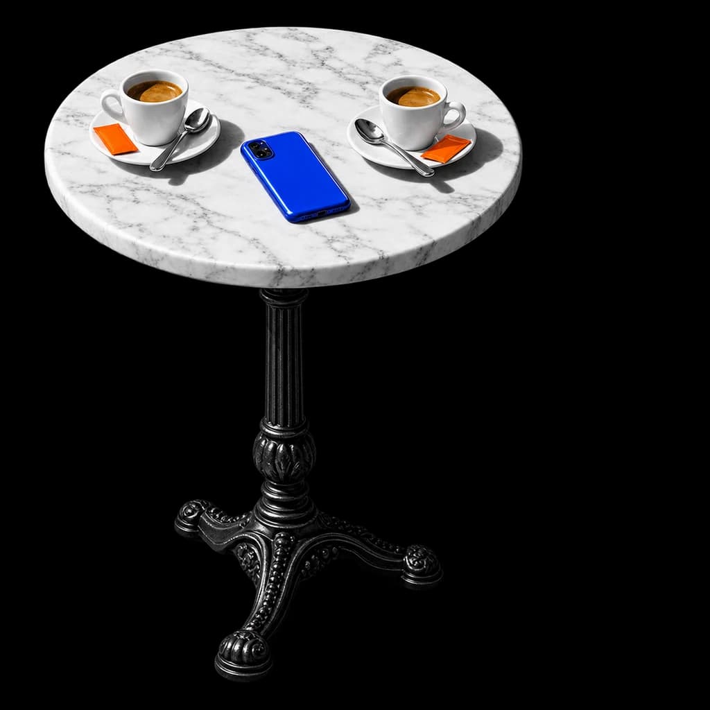 Un tavolino da bar in marmo con due tazzine di caffè una di fronte all'altra e un telefono blu in mezzo.